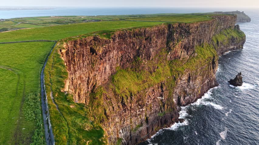 Majestic Cliffs of Moher rising vertically from the Atlantic Ocean on a misty day. Cinematic aerial drone footage of the rugged Irish coastline and crashing waves, County Clare, Ireland. 4K