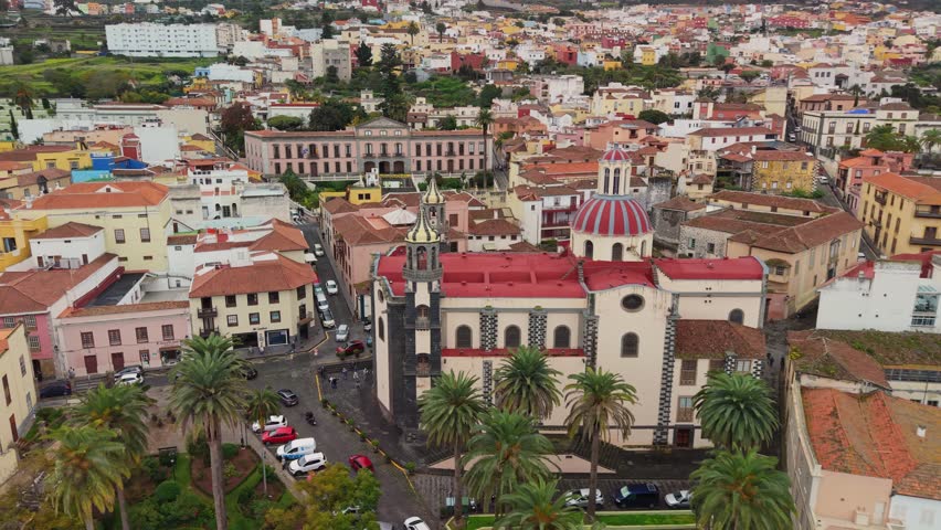 Stunning drone orbit around the Church of the Immaculate Conception in La Orotava. Majestic colonial architecture and red domes of the historic town under a cloudy sky, Tenerife, Canary Islands, Spain