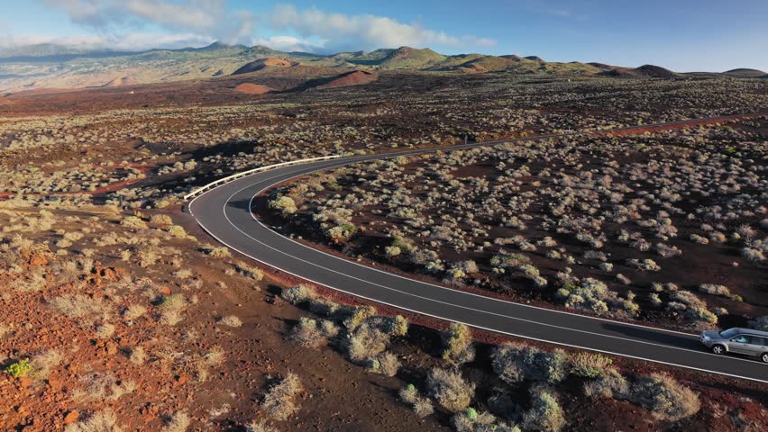 Car driving on winding asphalt road through the red volcanic desert of El Hierro. Exploring the remote island of El Hierro by car, lava fields, Canary Islands, Spain. Aerial drone view
