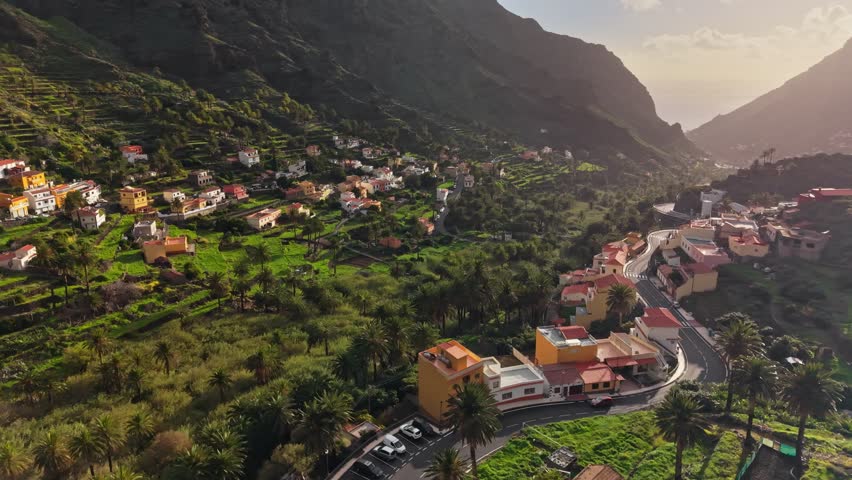 Magnificent aerial sunset view of Valle Gran Rey canyon with its iconic palm groves and terraces. Dramatic drone flyover of the volcanic mountains and deep valley, La Gomera, Canary Islands, Spain