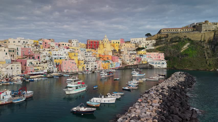 Spectacular wide-angle drone flyover of the ancient fortress and vibrant Corricella harbor. Majestic cinematic panorama of the colorful island architecture and turquoise sea, Procida, Naples, Italy