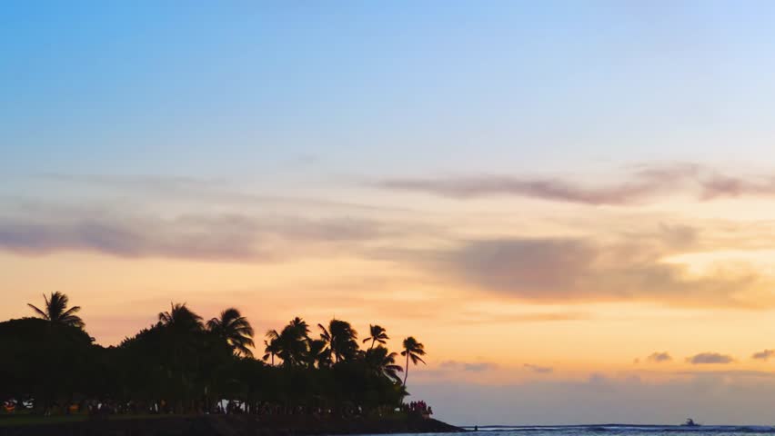 Tropical palm fringed coastline resort at sunset with cottage villa houses and vibrant skies over the ocean in Waikiki beach, Hawaii island