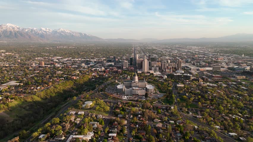 Stunning aerial view capturing Salt Lake City nestled among lush greenery, with dramatic mountains and snow-capped peaks in the background, reflecting a vibrant urban landscape.