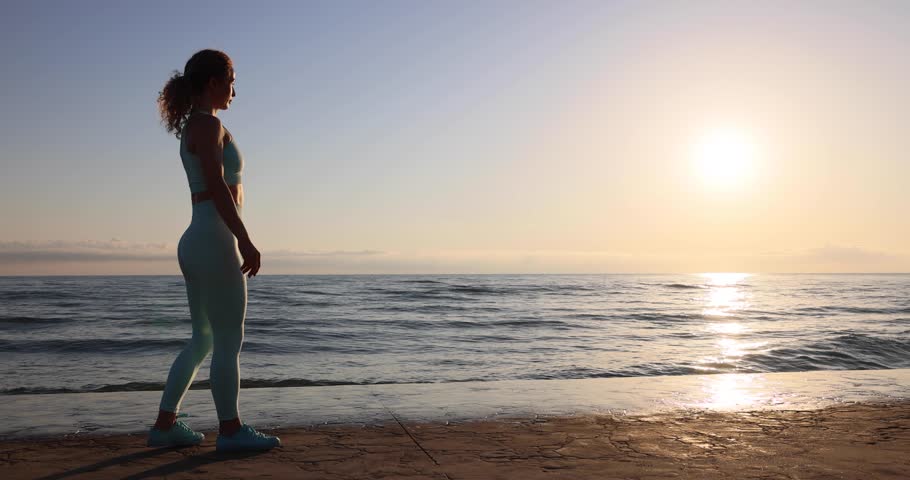 Fit young woman doing cartwheel at the beach during vacation. Sportive athletic female does a gymnastic exercise against sea and sky background. Summer sport and healthy lifestyle concept