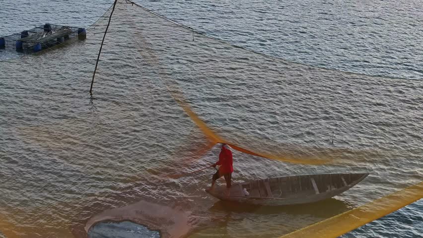 An aerial orbit shot reveals a lone Vietnamese fisherman working his large yellow net from a small wooden boat, showcasing traditional daily life on the serene waters of Vietnam.