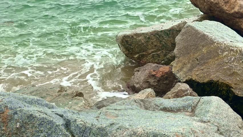 Clear seawater washing over large coastal rocks near a sandy beach shoreline.
