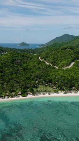 Hills with lush vegetation surrounding a turquoise bay and sandy shore under a bright sky. Shark Bay. Koh Tao, Thailand.