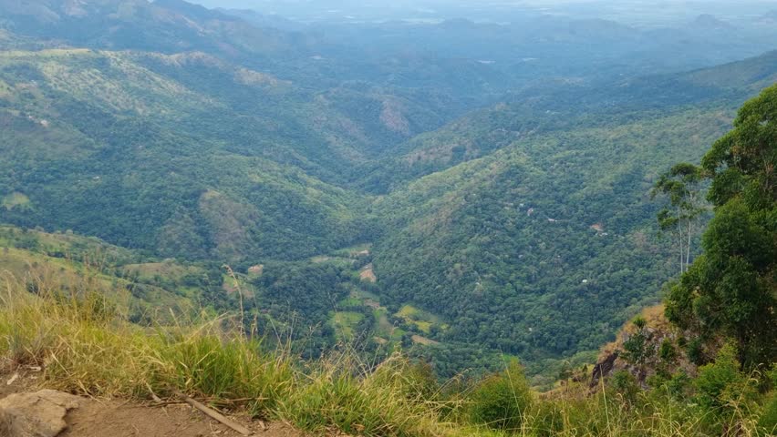 Panoramic view from Ella Rock in Sri Lanka, looking across Ambagaswatte Valley and misty mountain ranges beneath a cloudy sky, capturing the raw beauty and dramatic atmosphere of the hill country