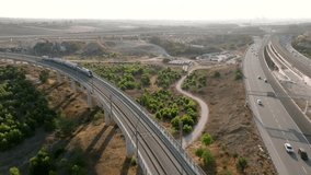 Aerial view of a modern passenger train crossing a high viaduct bridge over a busy highway in Israel. Cinematic 4K transportation and infrastructure footage. - Powered by Shutterstock - Get 15% off with code: PIKWIZARD15