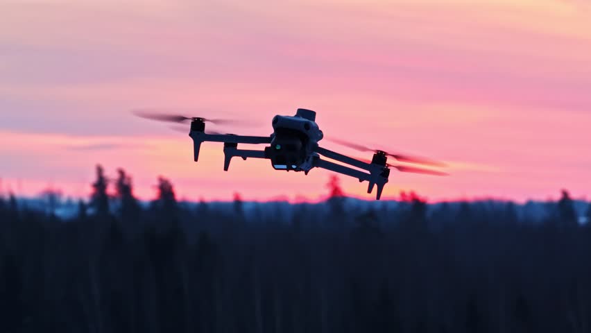 Modern drone flying low and a pink sunset behind. Close up