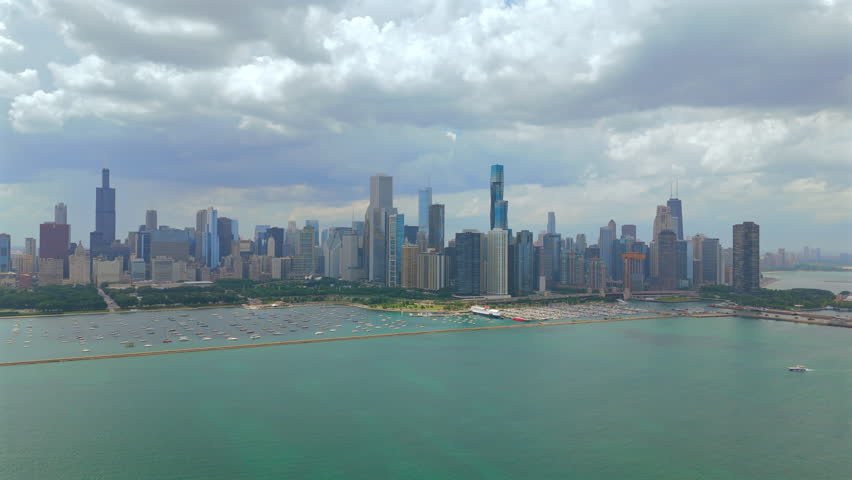 Chicago Illinois skyline captured from above showing dense downtown skyscrapers, green waterfront park and calm Lake Michigan, dramatic cloudy sky, wide urban panorama with modern architecture.