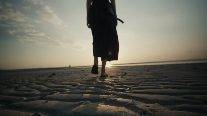 Woman walking barefoot on a sandy beach during sunset