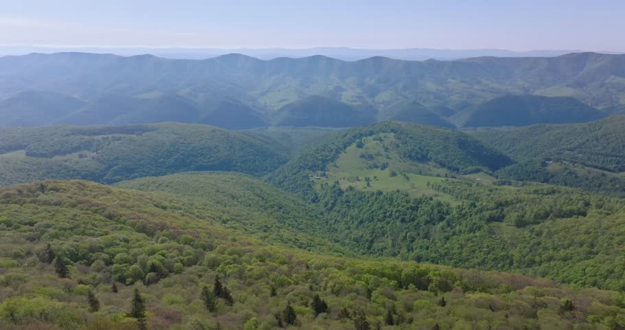 Wide aerial panorama establishing layered mountains and valleys around Spruce Knob in clear daylight, pullback