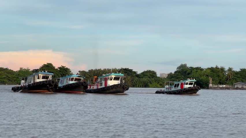 Close landscape view of working tugboats operating on the Chao Phraya River with green shoreline and urban Bangkok background.