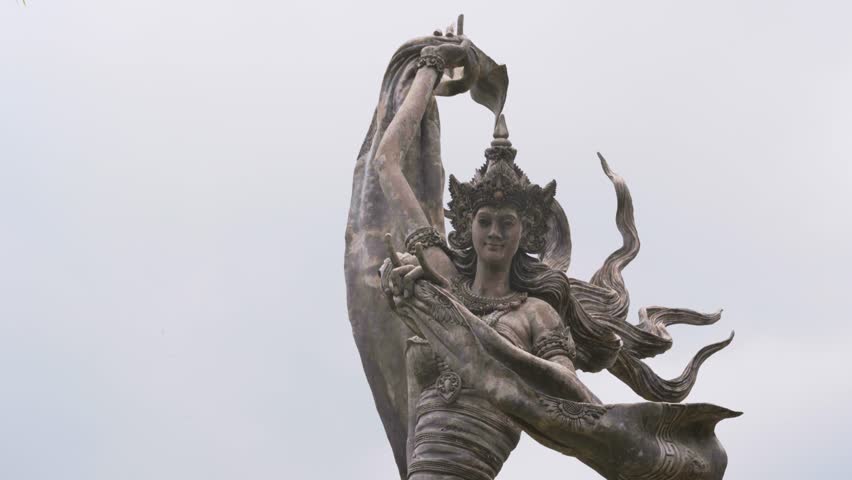 Cinematic footage featuring a smooth sliding-down camera movement along the iconic stone angel statues at Taman Dedari in Ubud, Bali, Indonesia.