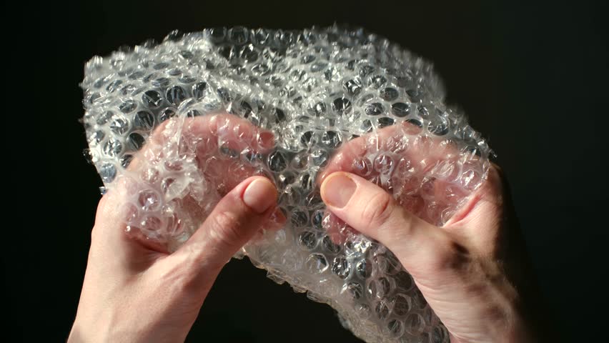 Hands popping bubble wrap on dark background, satisfying asmr, anti stress activity. Close up showing fingers bursting plastic packaging, creating relaxing sound. Popping bubble wrap for stress relief