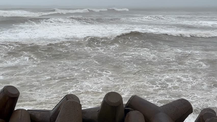 4K shot of a Dramatic motion of huge big waves smashing on concrete barrier wall that protects small marina at strong heavy winter storm in sea, early morning or evening low light time