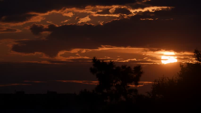 Dramatic sunset with clouds over silhouetted trees and buildings