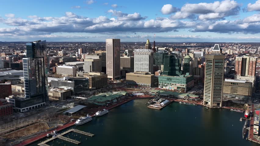 Aerial skyline view of Baltimore, USA, with the Inner Harbor, modern skyscrapers, waterfront piers and boats under bright blue sky with dramatic clouds. Wide shot.