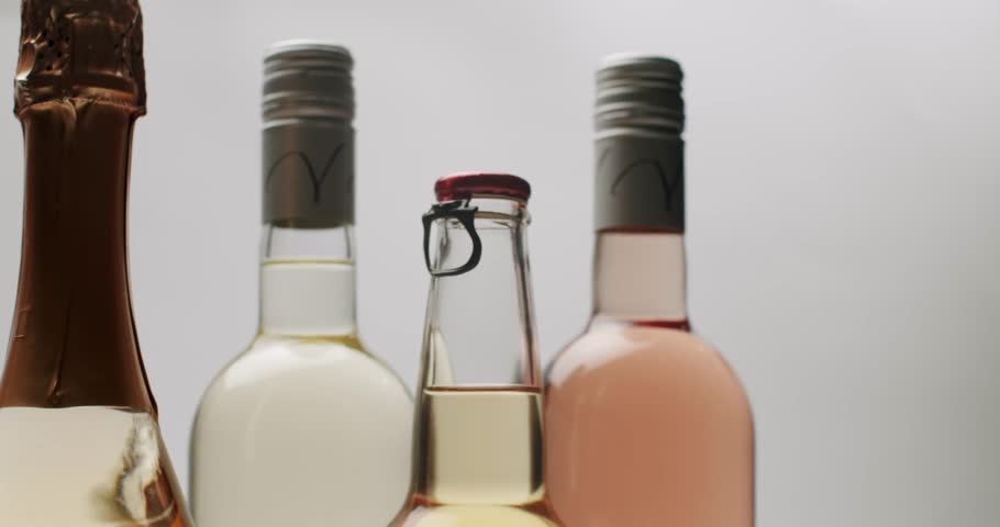 Various bottles containing different alcoholic drinks like cider, whiskey, and rose wine slowly rotating, isolated on a white background, highlighting their diverse shapes and colors.