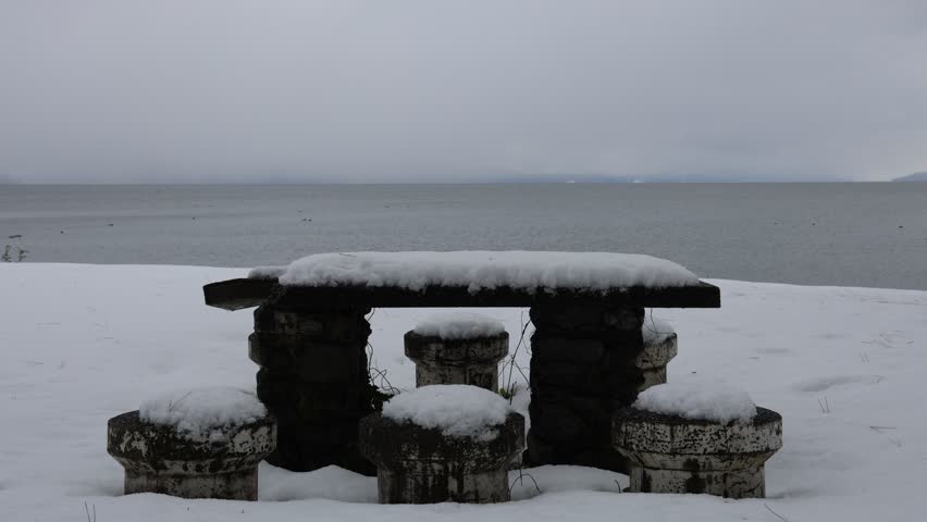 Snowy outdoor natural scene with a lake and stone chairs and a table