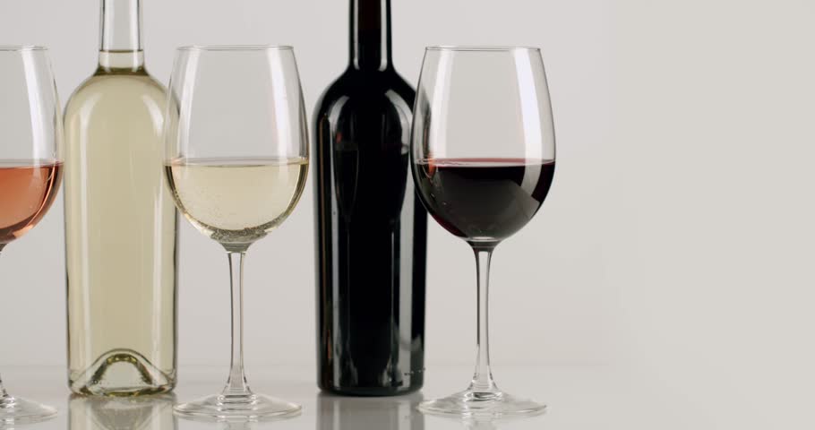 Selection of red, white, and rose wine bottles and glasses standing in a row, with the camera slowly panning from right to left, representing a wine tasting event or a cellar collection