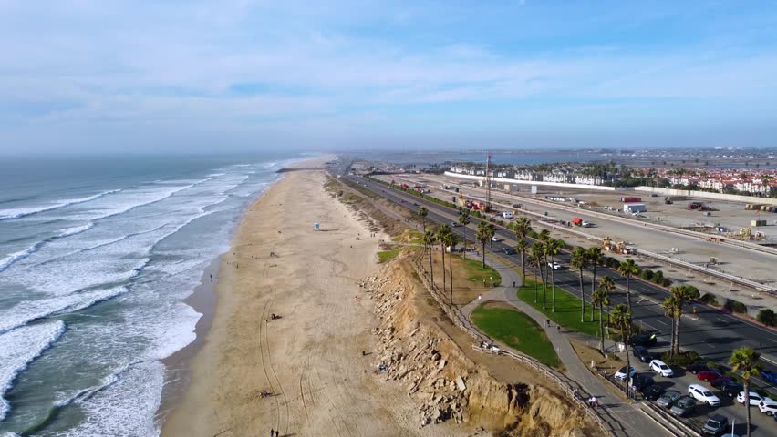 Road Tripping on Pacific Coast Highway 1. Cars Drive by Tropical Palm Tree at Sunset. Warm golden hour light and calm Ocean waves. Huntington Beach, Orange County, California