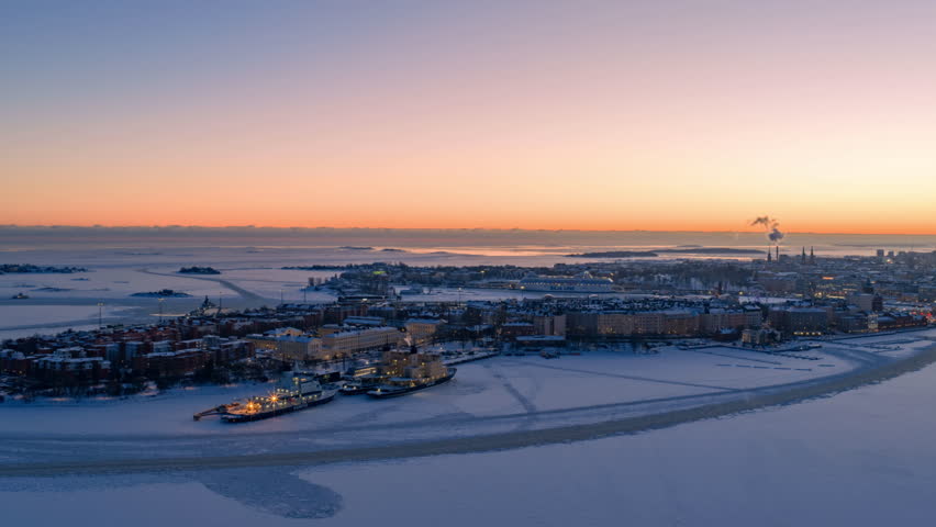 Drone hyperlapse Katajanokka blue hour Helsinki: frozen sea, Silja Line departure, snowy cityscape glowing. Crisp winter evening