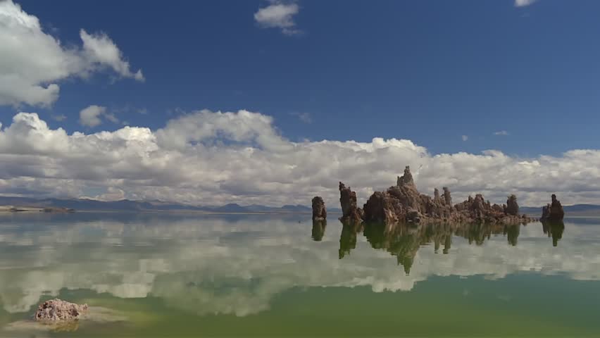 Sharp tufa formations reflected clearly in still green lake water with expansive clouds and mountains in background, Mono lake
