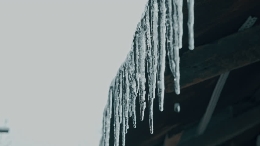 Icicles Descend From Old Wooden Overhangs. Long Ice Formations Hang Beneath Aged Barn Rafters In Winter