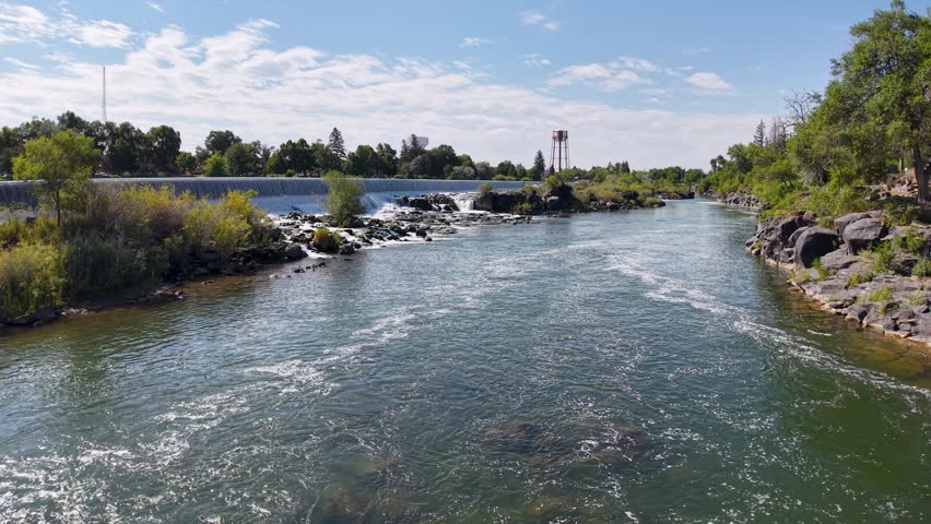 Aerial view of Snake River showing calm water flowing toward a small dam with green riverbanks, islands and distant structures under partly cloudy sky.