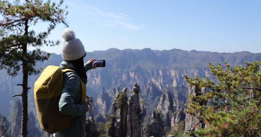 Female tourist taking selfie with smart phone hiking in mountains