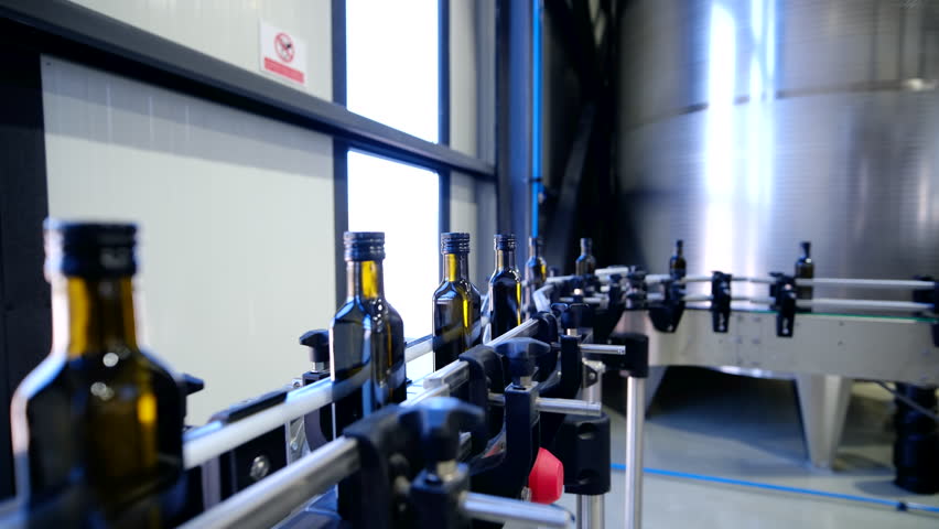 Close up of dark glass bottles moving on a conveyor belt during the automated filling and capping process in an industrial olive oil manufacturing plant