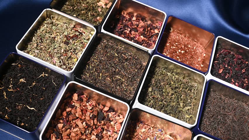 There are many varieties of tea in square iron jars in close-up on a blue background. Tea Shop
