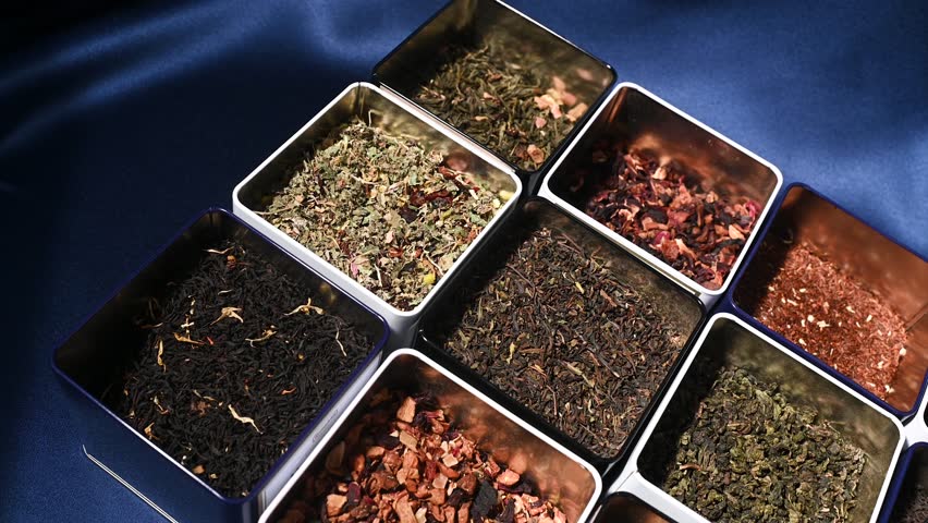 There are many varieties of tea in square iron jars in close-up on a blue background. Tea Shop