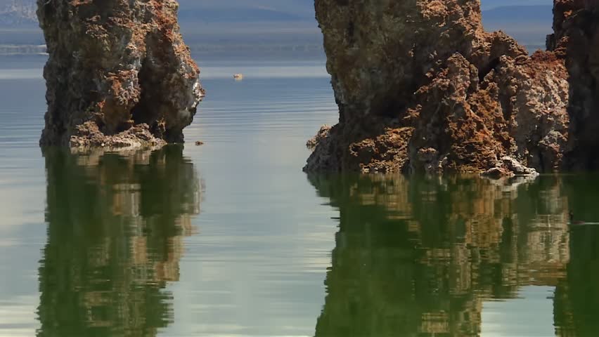 Two ducks glide across green water between towering tufa formations at Mono Lake, creating ripples in the reflections