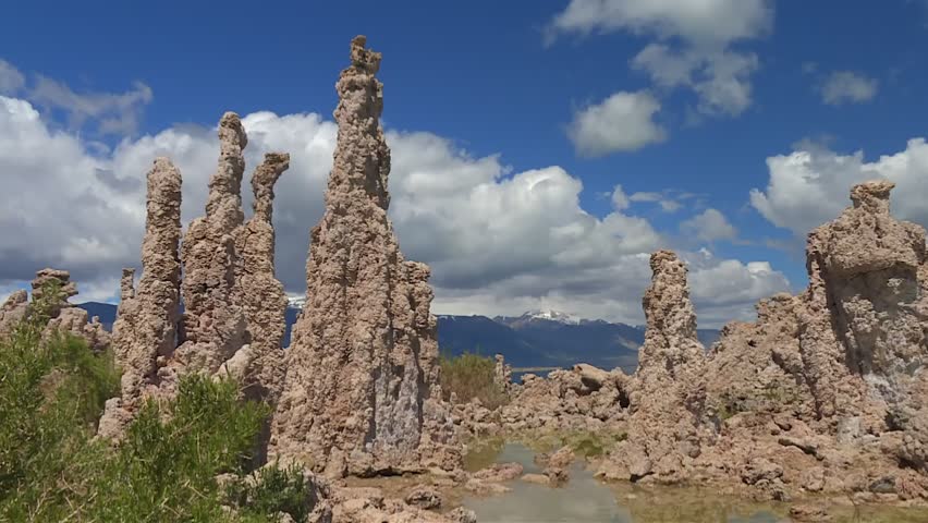 Towering tufa spires beside shallow water pools under a blue sky, with Twin Peaks visible in the far background at Mono Lake