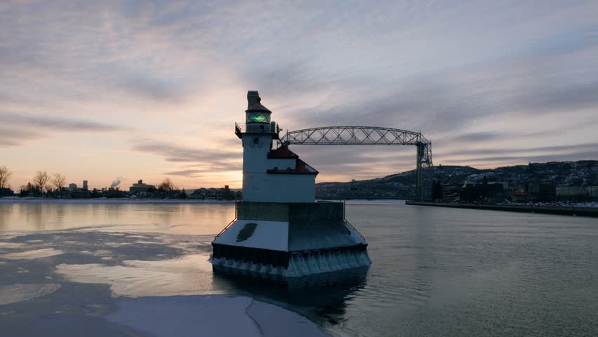 Cinematic drone reveal of the Duluth North Pier Lighthouse and Lift Bridge during a sub-zero winter sunrise with ethereal sea smoke on Lake Superior.