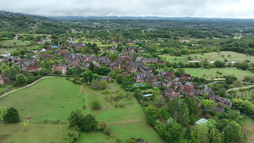 Aerial perspective of the medieval village of Collonges-la-Rouge showing traditional red stone houses surrounded by trees and pastoral landscapes in Nouvelle-Aquitaine.