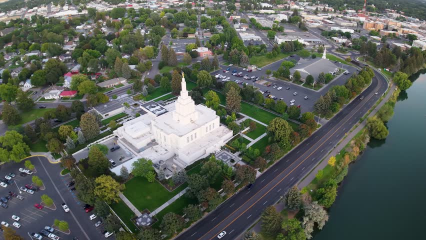 Aerial view of a white temple with a spire near the Snake River in Idaho Falls, surrounded by gardens, trees, and roads.