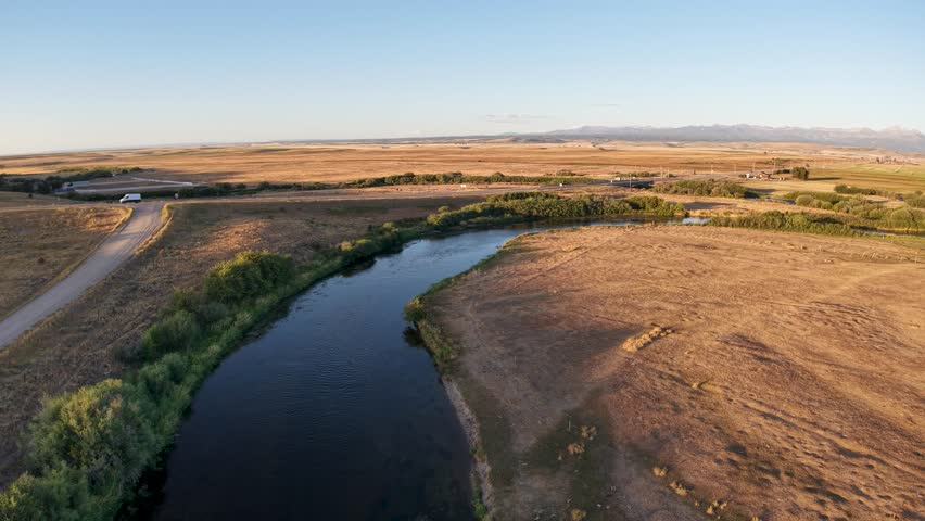 Aerial view of the Snake River winding through dry farmland in Idaho, with green vegetation along the riverbanks and golden-brown fields under a clear blue sky.