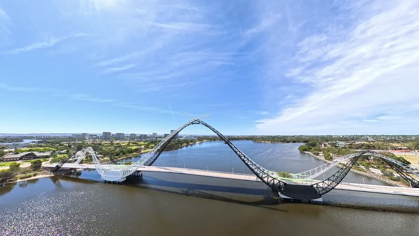An aerial view captures a striking arched Matagarup Bridge spanning calm Swan river with the modern Perth cityscape, Western Australia.
