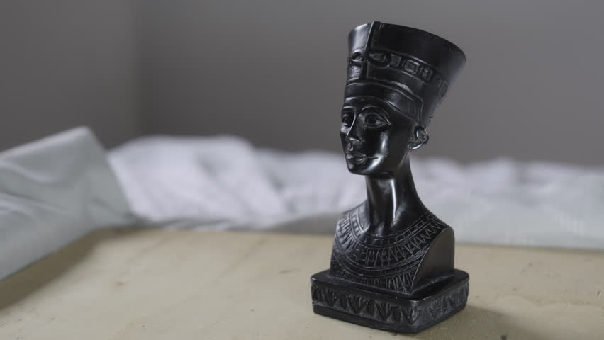 Black Egyptian queen bust sculpture inspired by ancient Egypt, featuring elegant facial features and a traditional headdress. Decorative statuette photographed in soft natural light with shallow depth of field and a neutral blurred background.