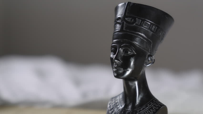 Black Egyptian queen bust sculpture inspired by ancient Egypt, featuring elegant facial features and a traditional headdress. Decorative statuette photographed in soft natural light with shallow depth of field and a neutral blurred background.