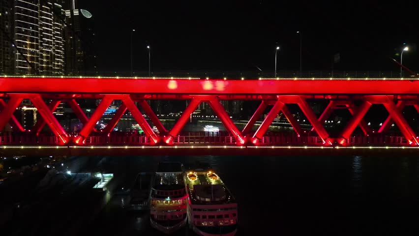 Red bridge glowing at night over river.