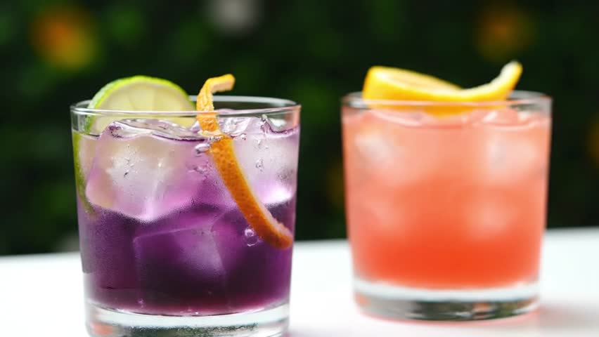 Two refreshing cocktails with citrus garnishes sit side by side on a table