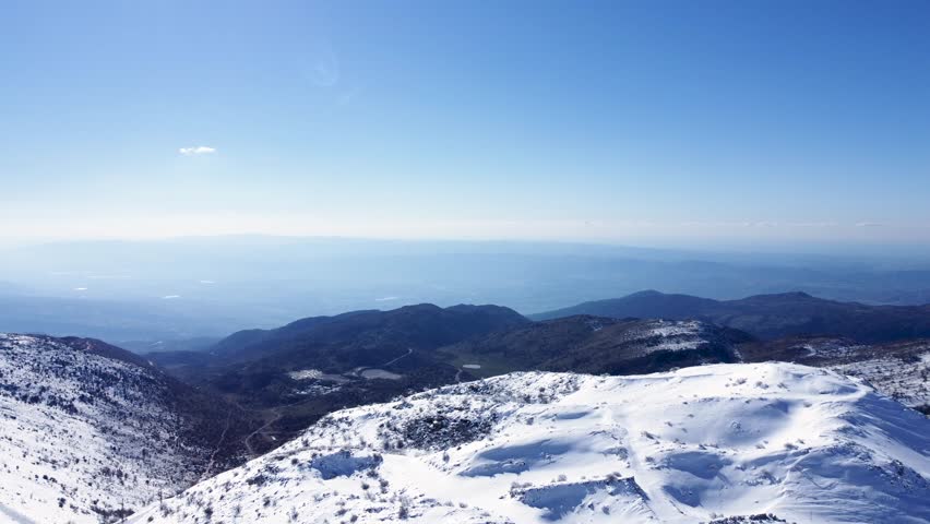 Stunning aerial view capturing the snow-covered terrain of Mount Hermon, revealing vast hills and valleys under a clear blue sky.