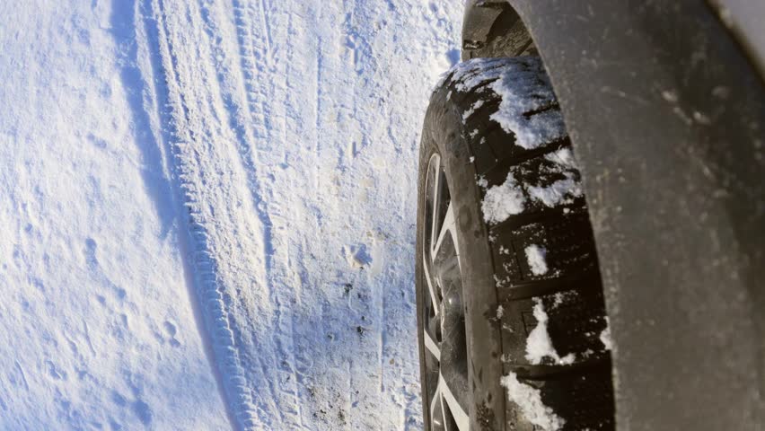 Close-up action shot of a car tire moving over a snowy road surface. Outdoor winter conditions and driving performance captured in daylight.