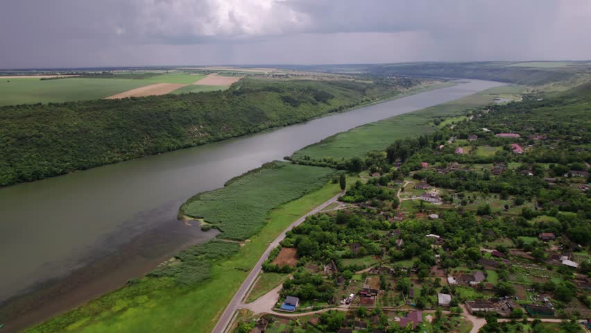Overcast Sky Over Tranquil River Village, Peaceful Village Nestled In Rolling Hills By Winding River