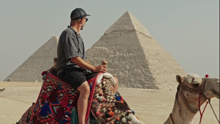 Classic Egyptian travel experience: a man sitting atop a camel at the Giza Plateau. The camel is adorned with a vibrant, traditionally patterned saddle.